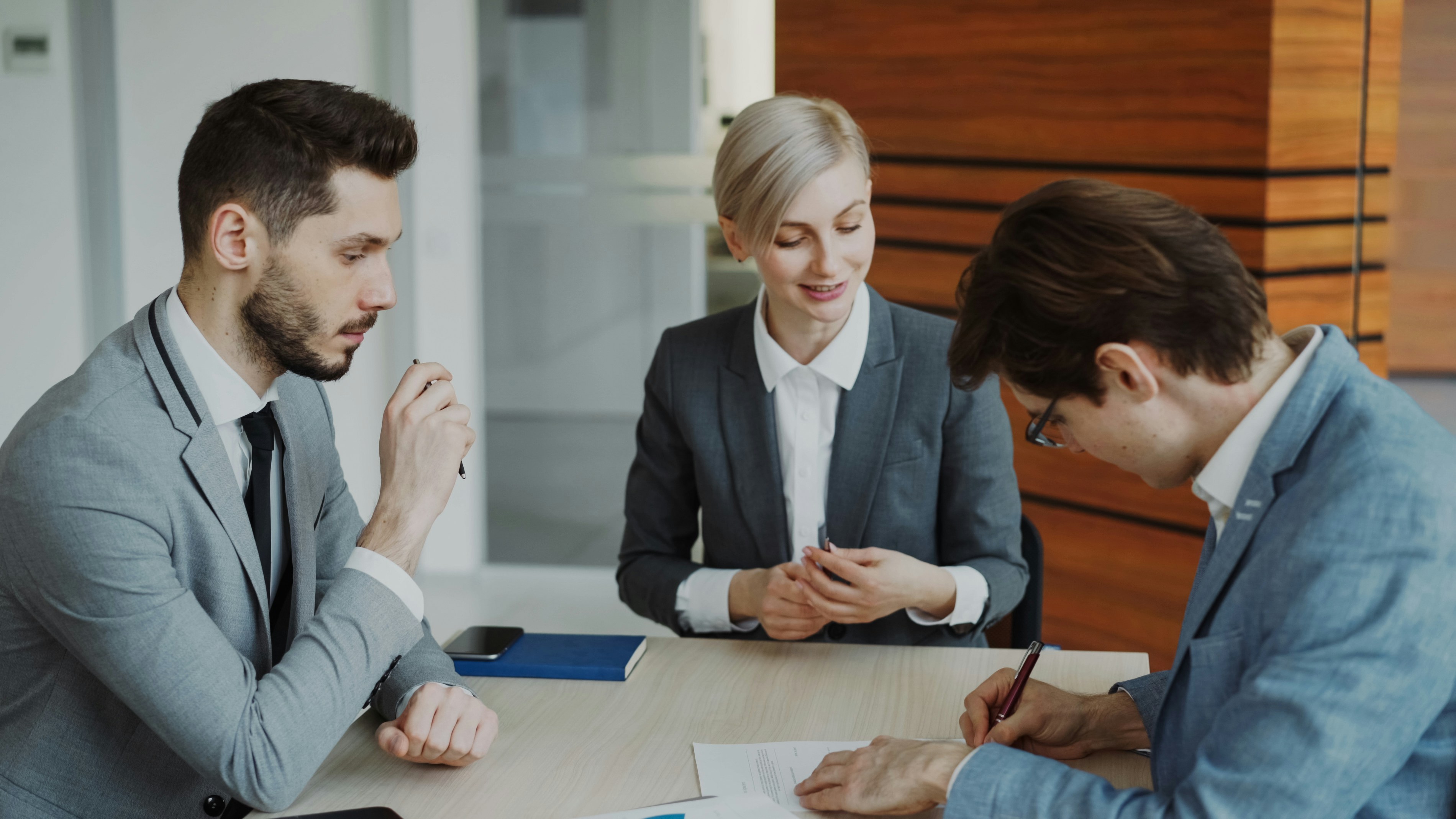 FULL 4K VIDEO for this still is in my bio link! ⬇️ Young businessman in suit signing contract with his colleague while corporate lawyer explaining details of partnership sitting in modern office indoors
